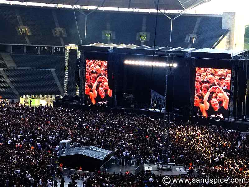 Fans visible on large stage screens during a massive rock concert at the Berlin Olympiastadion.